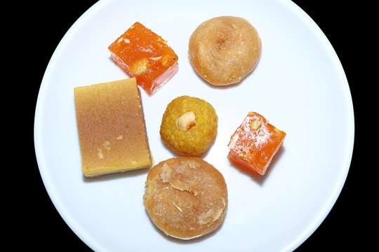 Indian sweets served in white plate. Halwa, badusha, ghee mysore pak, laddu in decorative plate, selective focus