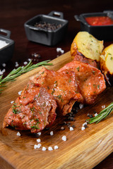 Grilled pork kebab with potatoes, on a wooden plate, decorated with herbs and tomato sauce.
