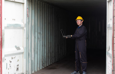 Young worker man with laptop at container terminal port warehouse for check stock product.