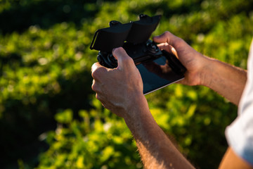 A young man in a white T-shirt has a drone controller in his hand. He operates a plane to record agricultural crops.