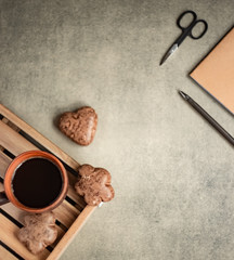 Brown coffee mug and chocolate chip cookies on a wooden tray, heart-shaped cookies and notebook and pencil