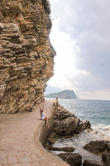 Girl travels in the mountains and rocks. Woman sits on the road under a rock and enjoys a vacation in Montenegro near Morgen beach on the wild nature. Hiking in a gorge with ocean or sea with surf