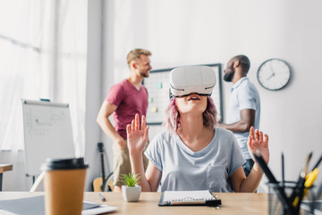 Selective focus of businesswoman using vr headset while businessmen talking in office