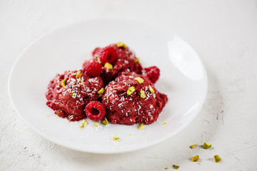Raspberry ice cream with aquafaba balls with pistachios on a white plate. Sugar, lactose, gluten free.