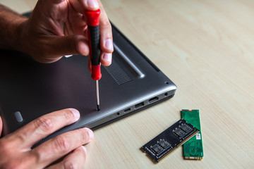 The laptop is located on the desktop. The computer service technician opens the lid with a screwdriver because he wants to install new components in it.