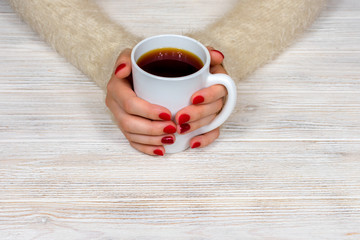 Female hands hold a white cup against the background of a white fluffy sweater with a beautiful red winter manicure. Drink, fashion, morning. New Year. Celebration. Tea coffee.