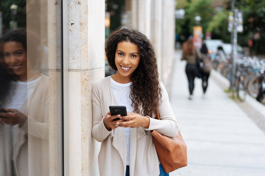 Smiling woman with phone standing in the street