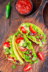 Taco shells with lettuce, ground beef meat,  mashed avocado, tomato, red onion and jalapeno pepper, on wooden board, vertical, top view