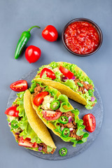 Taco shells on stone plate, with lettuce, ground beef meat,  mashed avocado, tomato, red onion and jalapeno pepper, vertical, top view