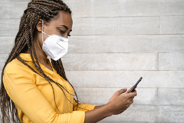 African woman wearing face medical mask using mobile smartphone - Young girl with braids having fun...