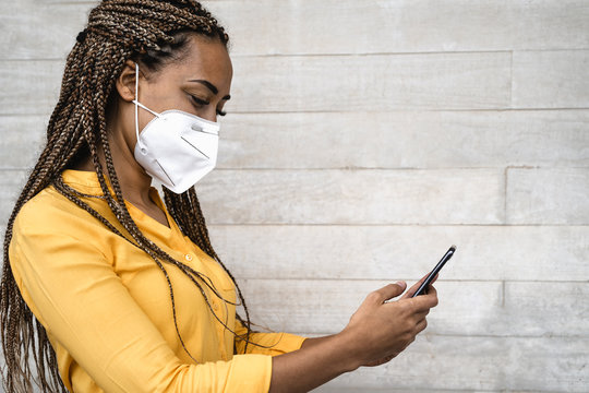 African woman wearing face medical mask using mobile smartphone - Young girl with braids having fun with phone during corona virus outbreak - Health care people and technology concept