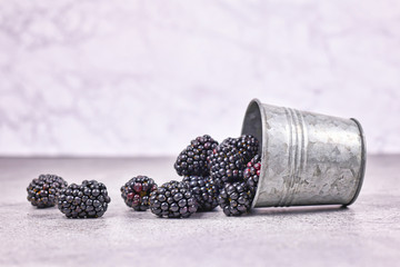 Fresh ripe blackberry fruits spilling out of iron cup