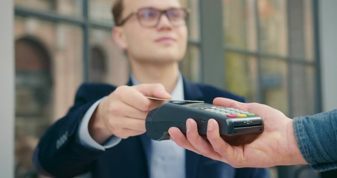 The businessman is taking out a credit card and paying for the order via a contactless payment terminal. Close-up shooting. Lunch break. 4K