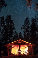 Wooden shelter and fireplace with starry night sky at background in Finland. - obrazy, fototapety, plakaty