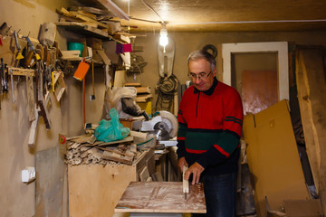 Satisfied cheerful joyful smiling woodmaster is standing near desktop in his workshop, workstation