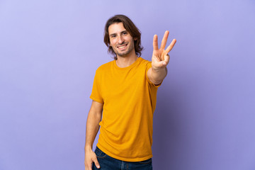 Young handsome man isolated on purple background happy and counting three with fingers