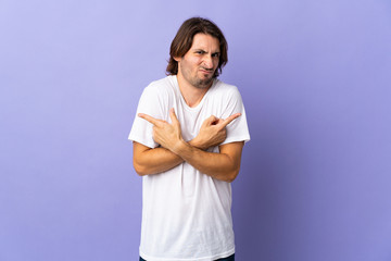 Young handsome man isolated on purple background pointing to the laterals having doubts