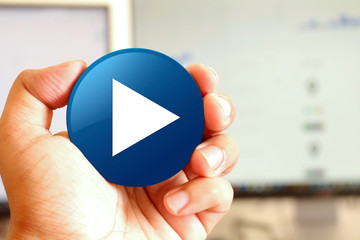 Play icon blue round button holding by hand infront of workspace background