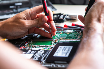 The service technician is trying to repair the laptop computer that is on his desk. He has a mobile...
