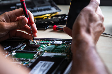 The service technician is trying to repair the laptop computer that is on his desk. He has a mobile phone in his hand on which he is watching how to do it.