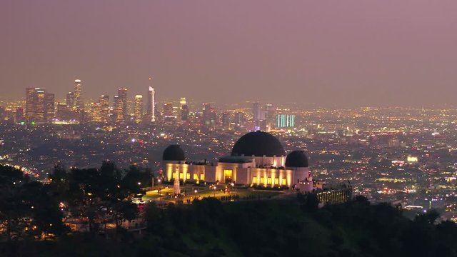 Aerial view of the Griffith Observatory, on Mount Hollywood, during night time, downtown Los Angeles in the background, in California, USA -  tracking, drone shot