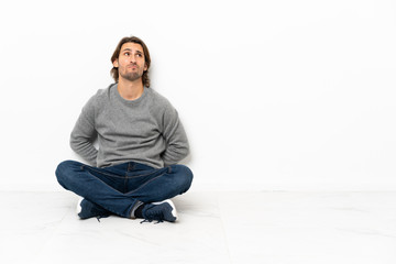 Young handsome man sitting on the floor over isolated background and looking up