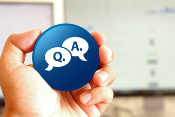 Question answer bubble icon blue round button holding by hand infront of workspace background