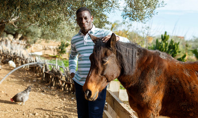African American male farm owner posing with horse at sunny day