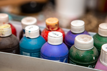 Box with bottles of acrylic paints of different colors. The bottles are dusty because they have not been used for a long time.