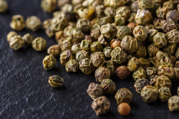 green peppercorns on dark slate stone background