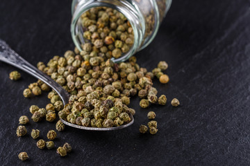 green peppercorns on dark slate stone background