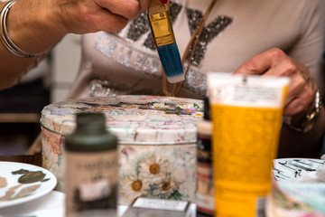 A woman's hand that arranges various flower motifs and thus makes a decoupage on a jewelry box. Copy space.