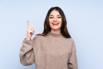 Young brunette woman wearing a sweater over isolated blue background pointing up and surprised