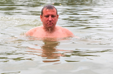 Water flows down the face of a young Caucasian man emerging from the lake