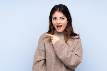 Young brunette woman wearing a sweater over isolated blue background surprised and pointing side