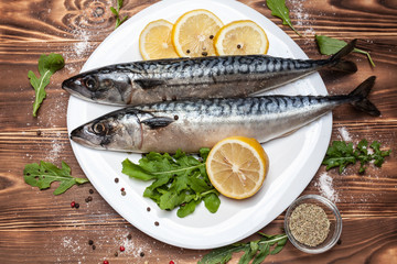 Raw mackerel with lemon, arugula, herbs and spices on white plate on wooden background.Healthy food  nutrition concept