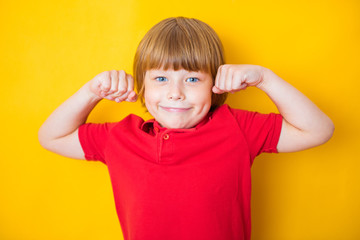 Portrait of a strong boy showing the muscles of his arms on yellow background