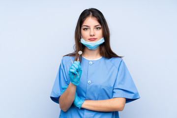 Woman dentist holding tools over isolated blue background keeping arms crossed