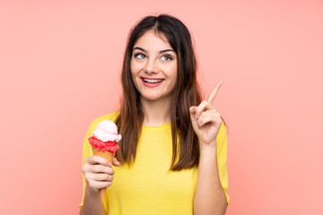 Young brunette woman holding a cornet ice cream over isolated pink background intending to realizes the solution while lifting a finger up