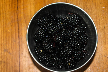 Fototapeta na wymiar Bowl of blackberries in metal bowl on brown table