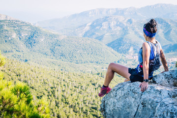 Naklejka premium Woman runner climbing a mound of rocks looking at the mountains.