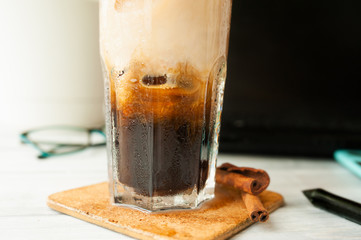 wet glass with iced coffee and drops close-up on workplace background