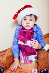 little cute boy with Christmas gifts at home wearing red Santas hat. closeup emotional happy smiling in mess with toys, lifestyle holiday people concept