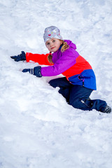 Fototapeta na wymiar Outdoor winter portrait of little cute girl wearing ski clothes.Girl climbing a snow slide. Stylish clothes for kids.