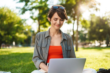 Image of pleased student girl smiling and doing homework with laptop