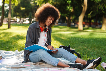 Image of pleased african american girl writing in exercise book