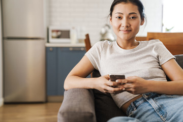 Pretty asian girl using smartphone on the couch at home