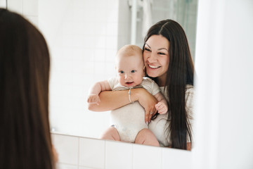Photo of excited mother with her baby smiling and looking at mirror