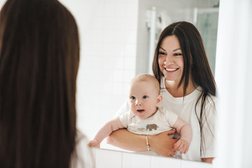 Photo of excited mother with her baby smiling and looking at mirror