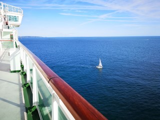 An ocean liner passes a yacht on a vibrant blue sea - over looking a safety hand rail.